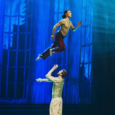A man and a woman are performing a dance act. The woman appears to be floating in the air above the man.
