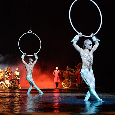 Aerial hoop acrobats dance across the top of the water covering the stage - O