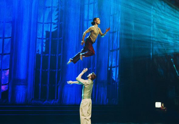 A man and a woman are performing a dance act. The woman appears to be floating in the air above the man.